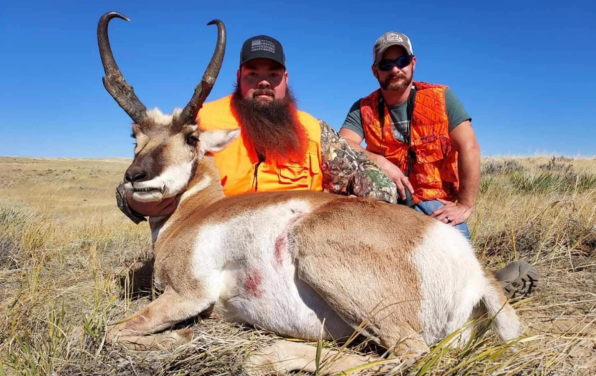 A hunter and his friend posing with his trophy antelope in the grass
