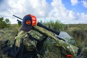 Hunting backpack with a rifle and baseball cap laying on it in the sagebrush