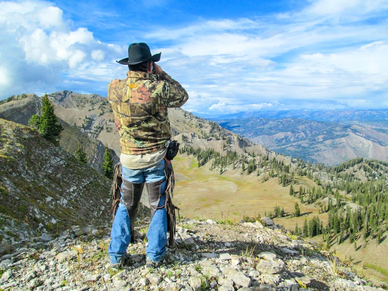 man in a cowboy hat glassing for big game standing at the top of the mountain peak in wyoming